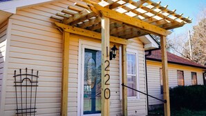 A house with a wooden pergola over the front door, a number '1220' on the door, and a metal gate to the left.