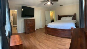 A bedroom with a wooden bed, a dresser, a television mounted on the wall, and a ceiling fan. - Home away from home (Auburndale)