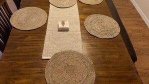A wooden dining table with six woven placemats and a central placemat, surrounded by wooden chairs. - Home away from home (Auburndale)