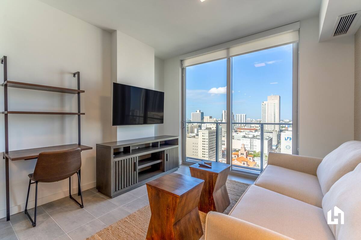 Una sala de estar moderna con un televisor grande, un sofá, un escritorio y vistas a la ciudad.