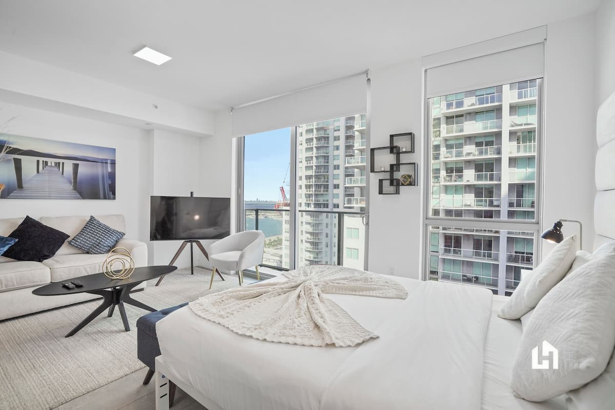 Una habitación de hotel moderna con una cama grande, televisión, sofá y balcón con vista a la ciudad.