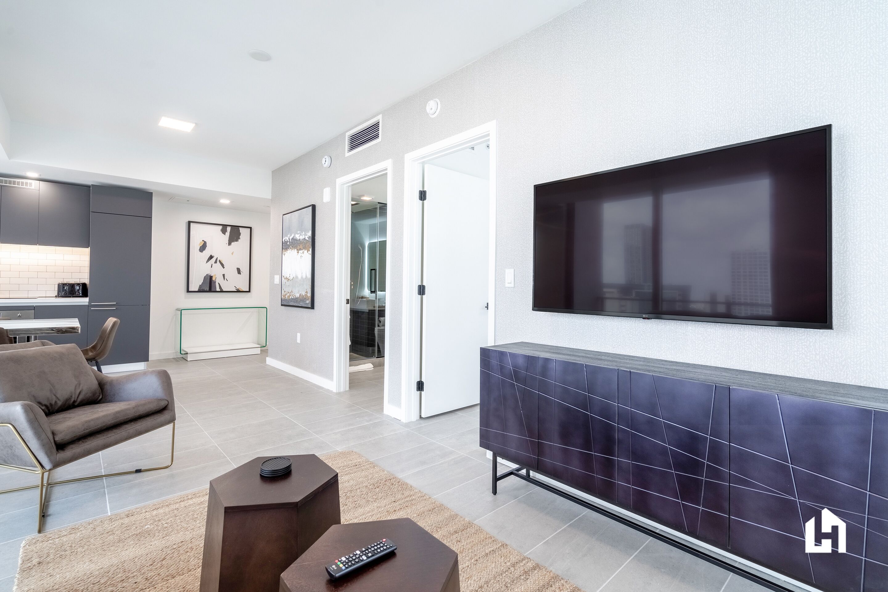 Un salon moderne avec un téléviseur à écran plat, un canapé, une table basse et une cuisine en arrière-plan.