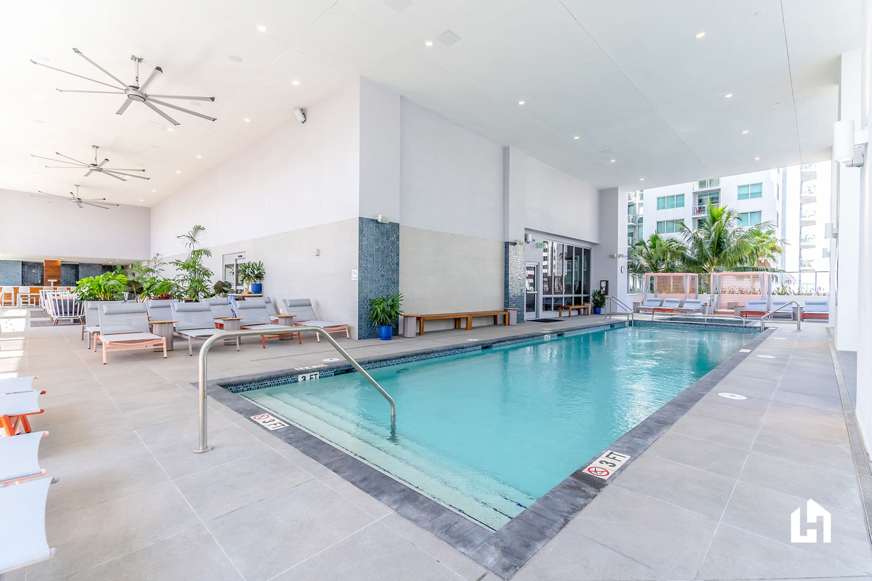 An indoor swimming pool with lounge chairs, a bench, and ceiling fans.