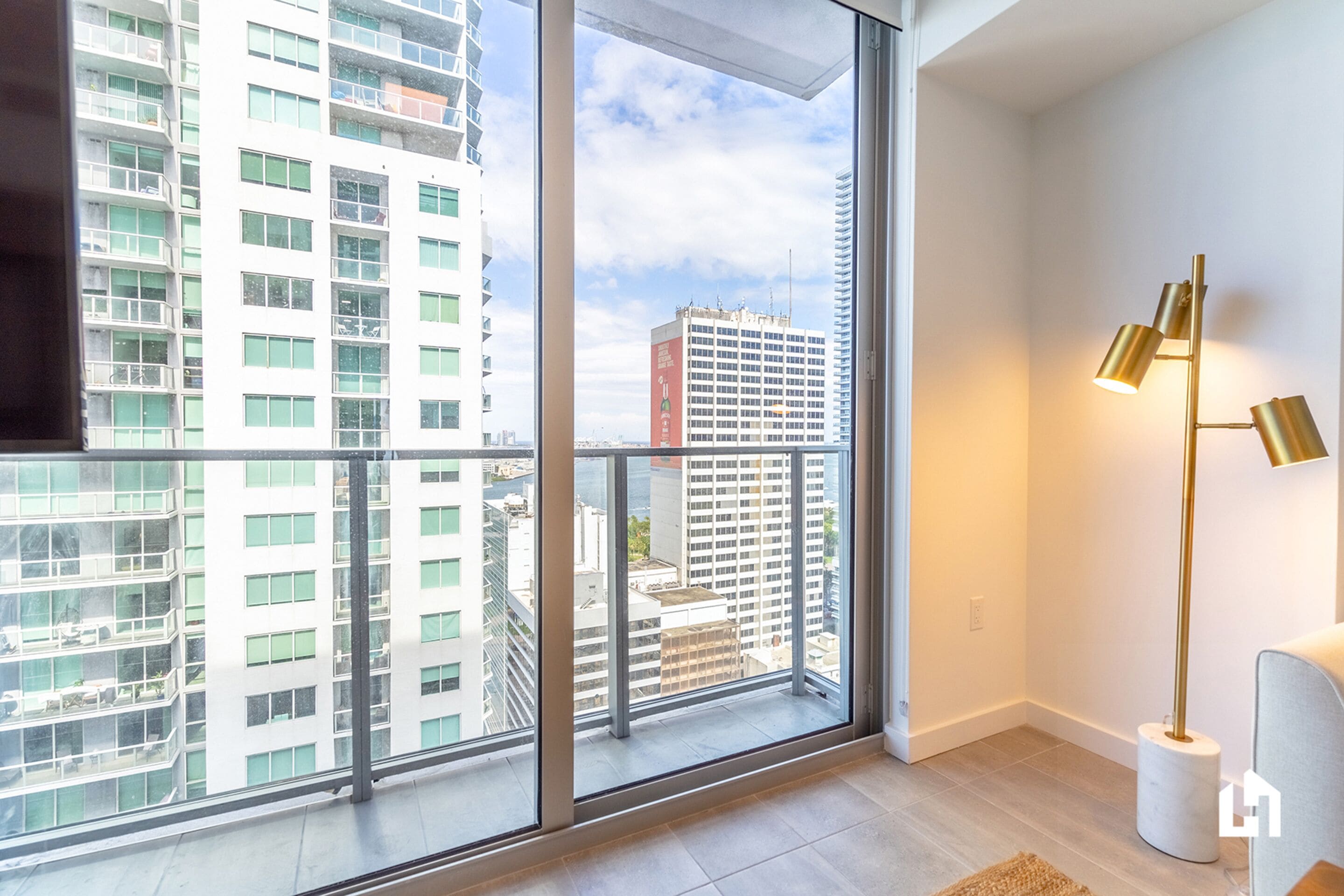A modern apartment with large floor-to-ceiling windows, a minimalist floor lamp, and a view of high-rise buildings.