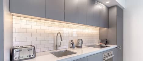Une cuisine moderne avec des meubles gris, un plan de travail blanc, un grille-pain, une bouilloire et un évier.