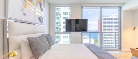 A modern hotel room with a large bed, a flat-screen TV, and a balcony with a city view.