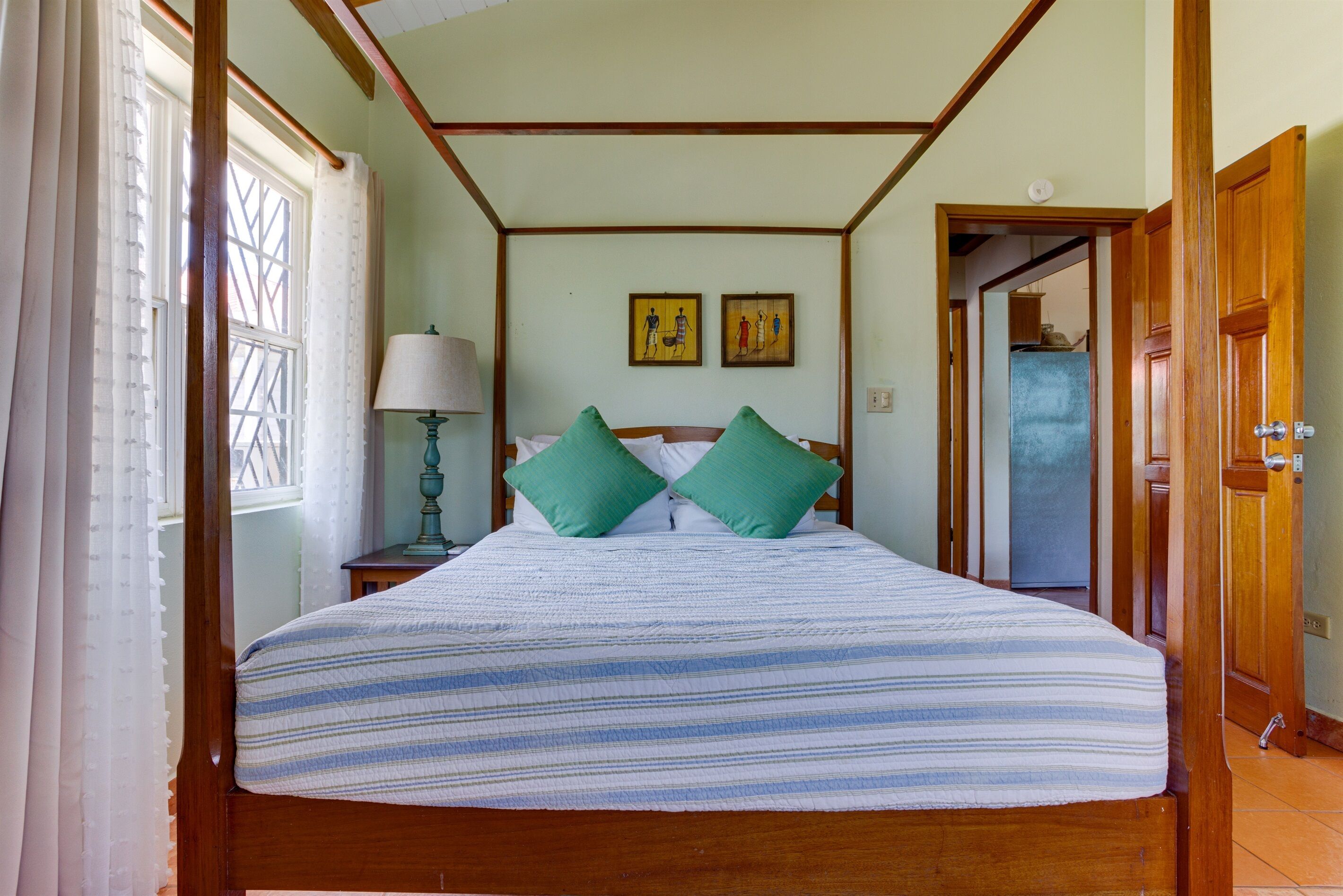 Un dormitorio con cama de madera, almohadas verdes, una mesita de noche con lámpara y dos cuadros en la pared.