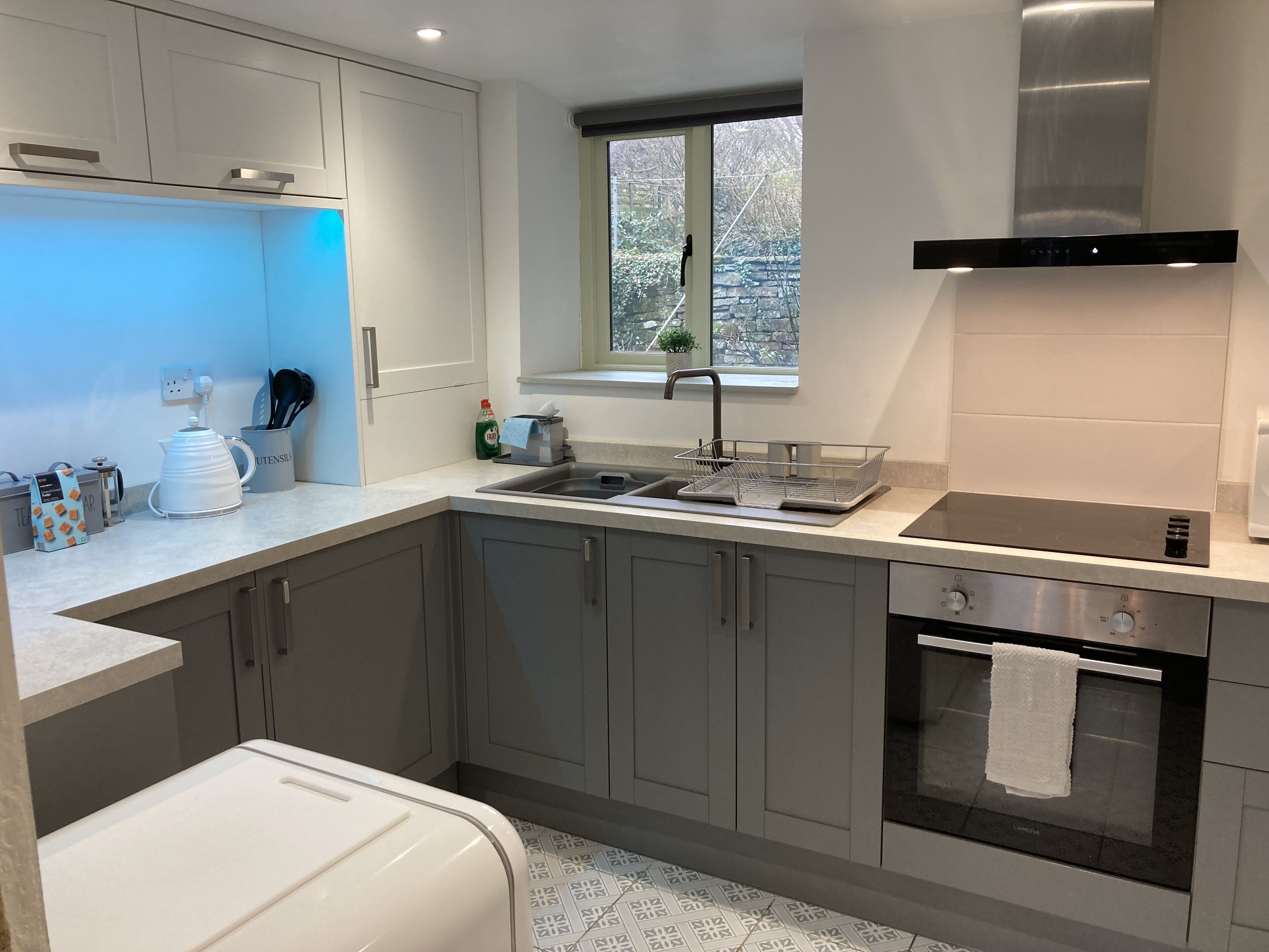 Une cuisine moderne avec des meubles gris, un évier en acier inoxydable et un four.