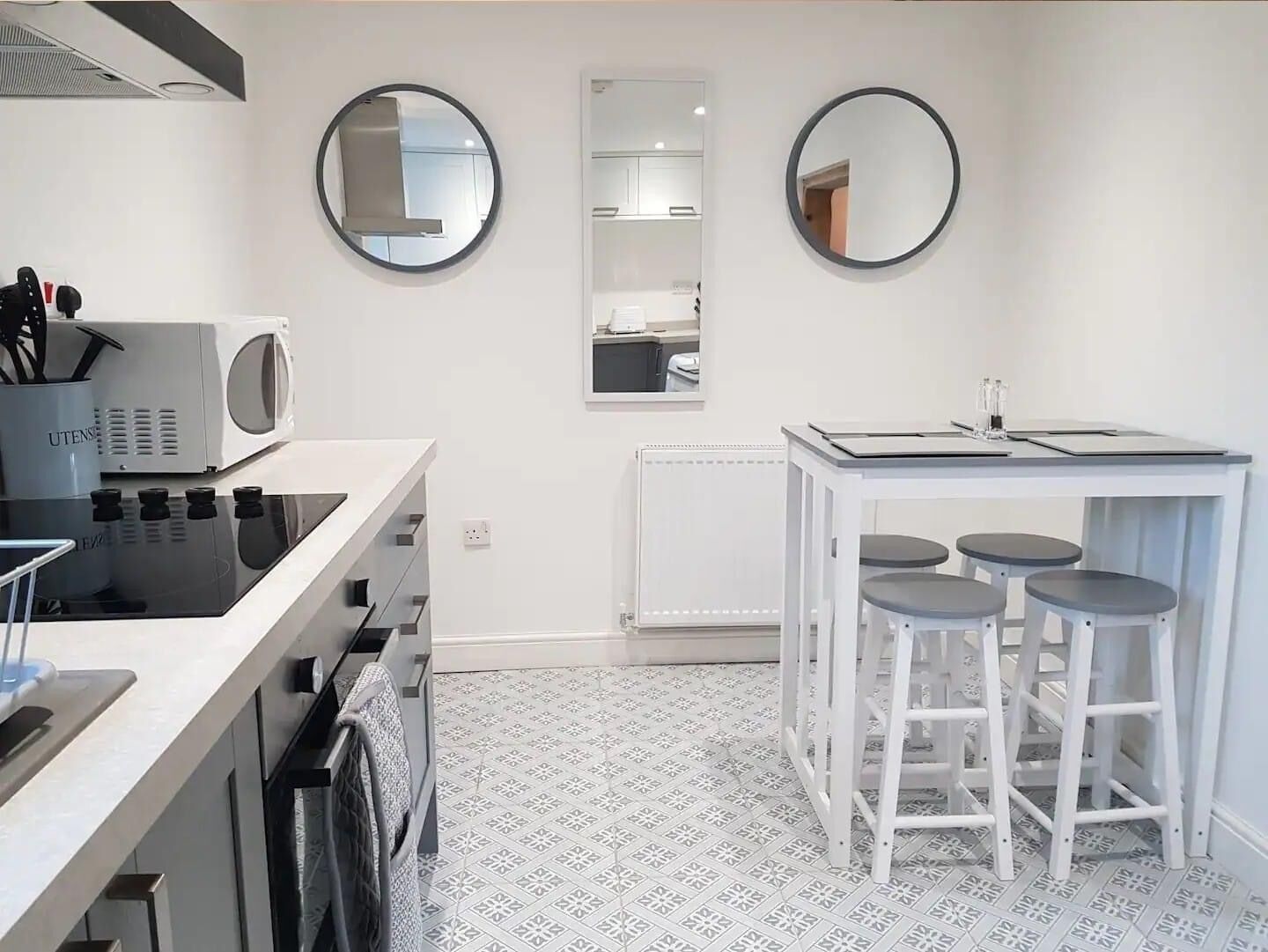 A modern kitchen with a microwave, stove, and sink. There are two round mirrors on the wall and a small bar area with stools.