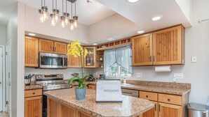 A modern kitchen with wooden cabinets, a granite countertop, a stainless steel stove, and a welcome mat. - Relaxing Pool & Hot Tub House near RIT Inn (West Henrietta)