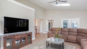 A living room with a flat-screen TV, a brown sofa, a coffee table, and a ceiling fan. - Relaxing Pool & Hot Tub House near RIT Inn (West Henrietta)