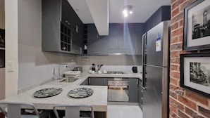 A compact kitchen with dark cabinets, a stainless steel refrigerator, a built-in oven, and a granite countertop. - Unique Apartment-1/BR-1/BATH-Miraflores- Ocean/Park-Views (Lima)