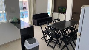 A modern living room with a black sofa, a dining table with chairs, a TV, and a balcony with a pool view. - Vila Bangalô (São José da Coroa Grande)