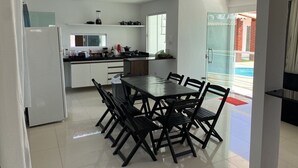 A modern kitchen with a dining area, white cabinets, a black dining table, and a refrigerator. - Vila Bangalô (São José da Coroa Grande)