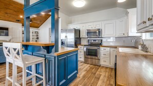 Eine moderne Küche mit weißen Schränken, einer blauen Akzentwand, Edelstahlgeräten und einer Holztheke mit Barhocker.