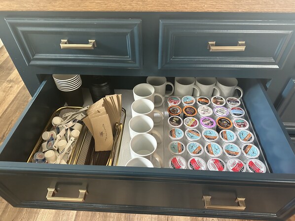 A drawer with compartments containing various items including coffee cups, coffee pods, and paper bags.