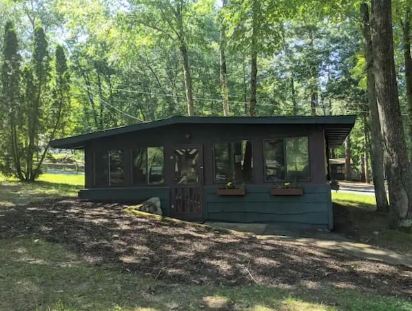 Une petite cabane à un seul étage, dotée d’un toit en pente, de grandes fenêtres et d’un porche agrémenté de jardinières.