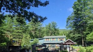 A lodge with a green roof, surrounded by trees and a fenced garden area with benches.