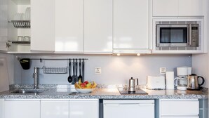 Una cucina moderna con mobili bianchi, un lavello in acciaio inossidabile, un forno a microonde, una macchina da caffè e un tostapane.