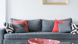 Un divano grigio con cuscini decorati, un tavolino da caffè in vetro e uno specchio con cornice dorata sulla parete.