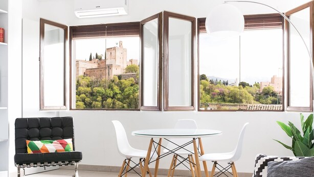Un soggiorno moderno con zona pranzo, ampie finestre con stipiti in legno, un divano nero, sedie bianche e un tavolino.