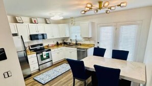 A compact kitchen with white cabinets, a built-in oven, and a dining area with a wooden table and blue chairs. - Escape to Comfort in Lexington/Hamburg: Stylish 3BR/2.5BA Home (Lexington)