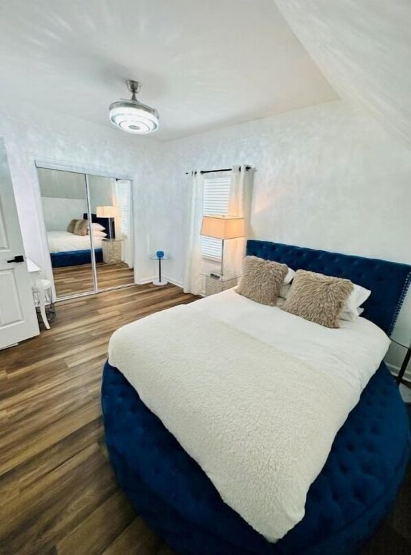 Relax in this serene bedroom with a large bed, ceiling fan, and mirror above.