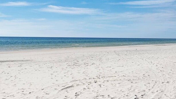 Ein weiter Sandstrand mit Fußspuren, die zum Wasser führen.