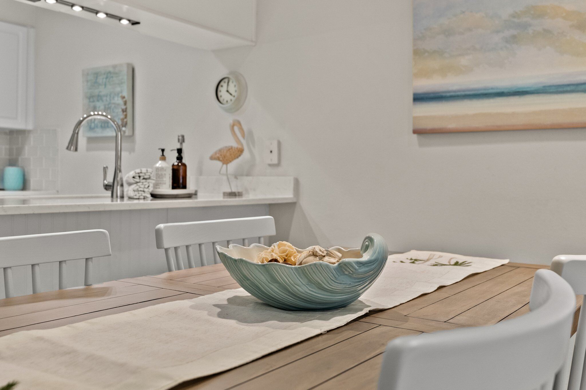 A modern kitchen with white cabinets, a white countertop, and a blue ceramic bowl on a wooden table.