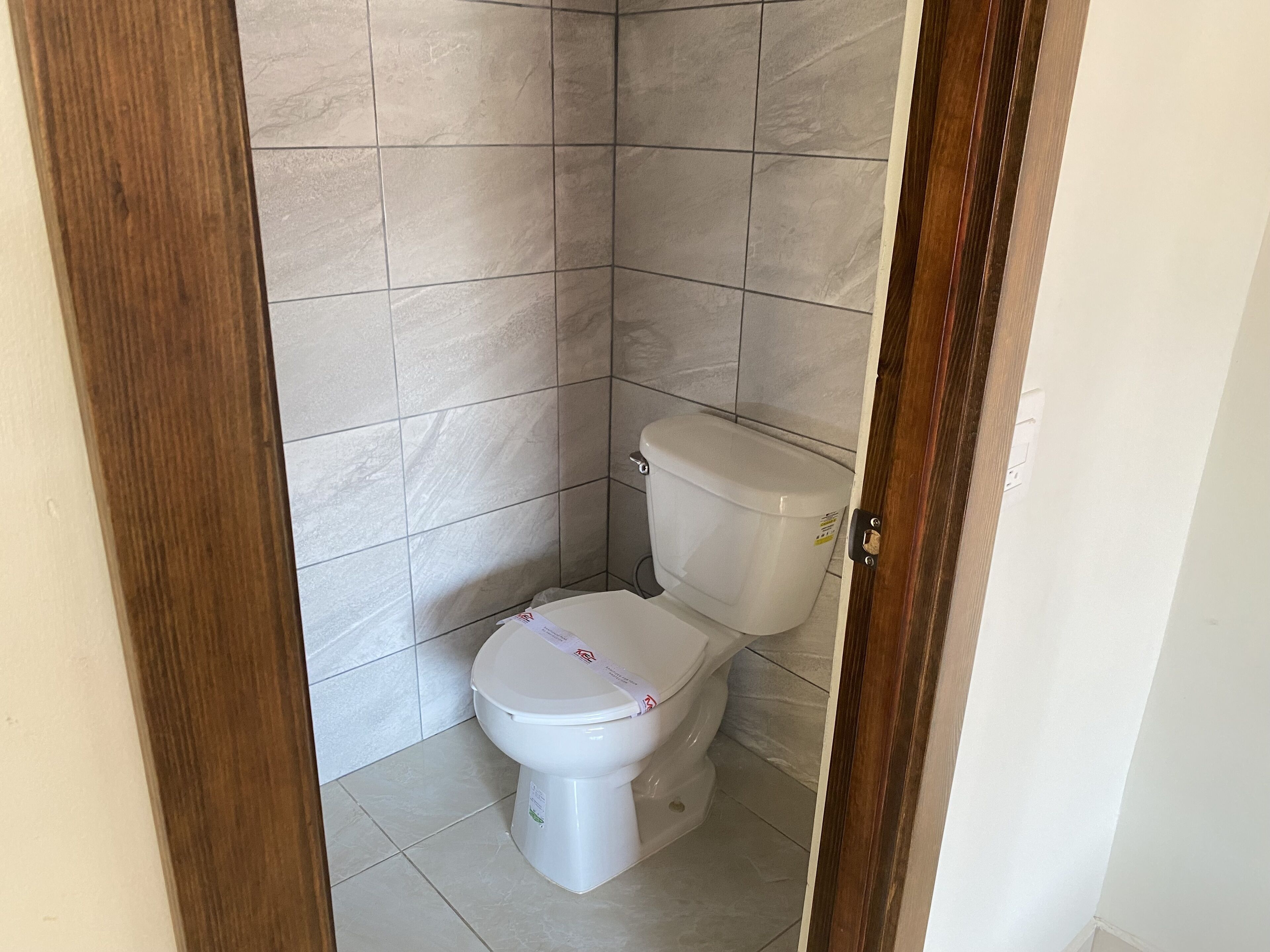 Ein kleines, sauberes Badezimmer mit weißer Toilette, gefliesten Wänden und einer Holztürrahmen.