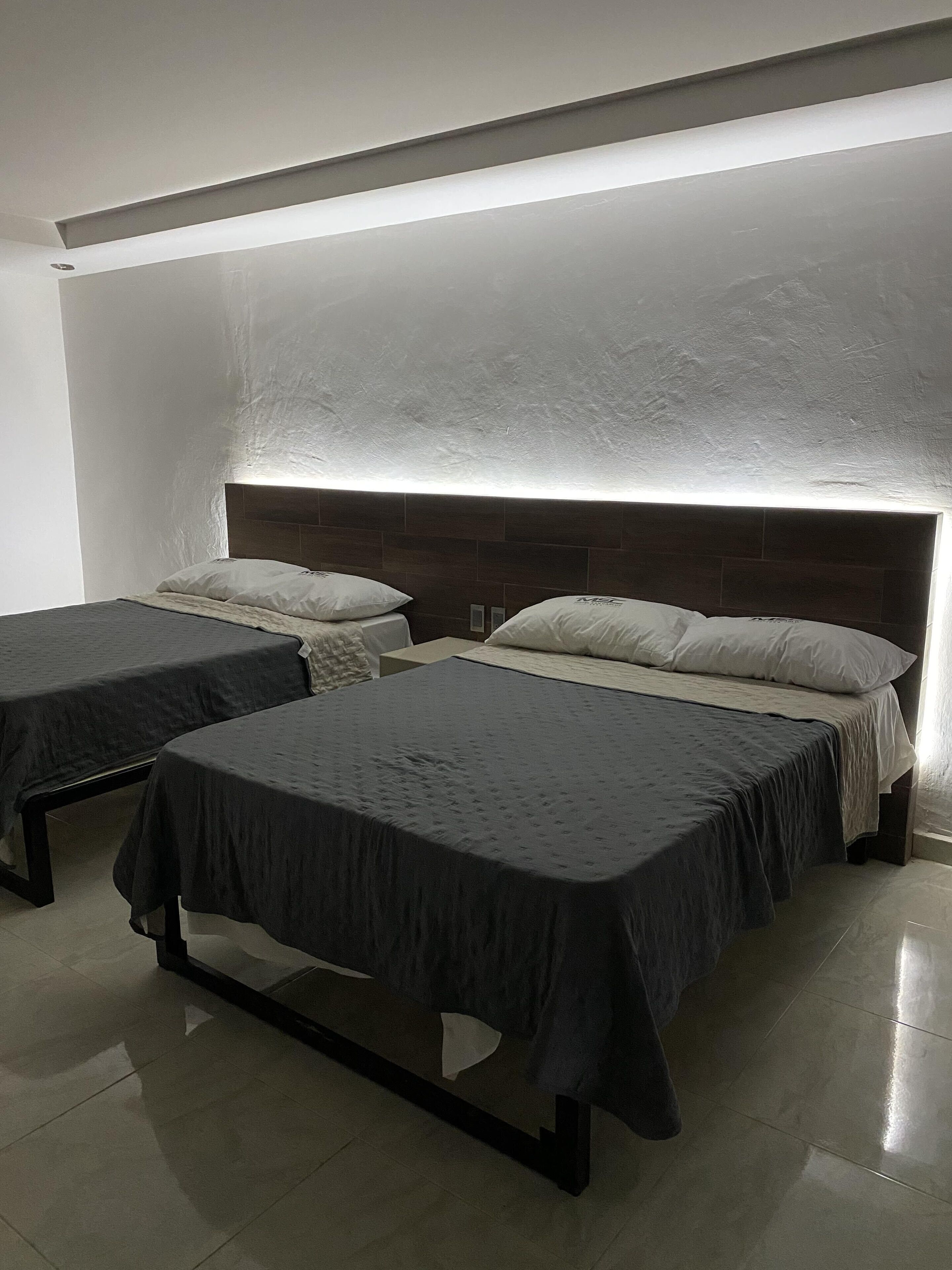A bedroom with two single beds and a larger bed, all with dark bedding. The room has a modern design with a textured ceiling and a wooden headboard.