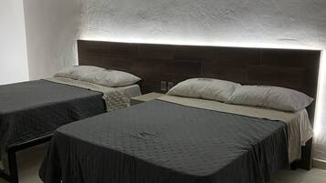 A bedroom with two single beds and a larger bed, all with dark bedding. The room has a modern design with a textured ceiling and a wooden headboard.