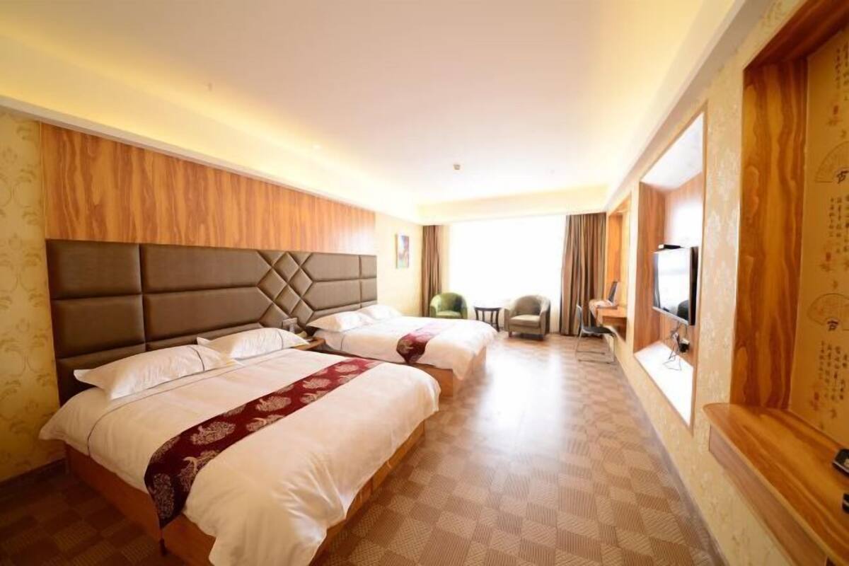 Una habitación de hotel con dos camas, televisión, una mesita y una ventana con cortinas.