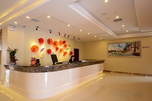 Zona de recepción de hotel con mostrador de mármol, una recepcionista y un muro decorado con motivos florales.