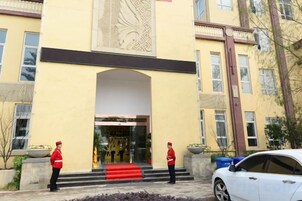 A hotel entrance with a red carpet, two security personnel, and a white car parked outside.
