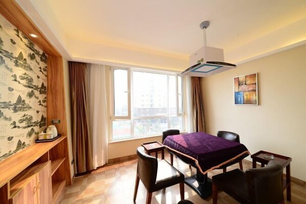 A hotel room with a bed, two chairs, a small table, a desk, a window with curtains, a wall-mounted air conditioner, and a shelf with items. - Nuoman Holiday Hotel (Xiantao)
