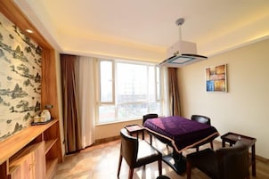 Una habitación de hotel con cama, dos sillones, una mesita, un escritorio, una ventana con cortinas, un aire acondicionado instalado en la pared y una estantería con objetos.