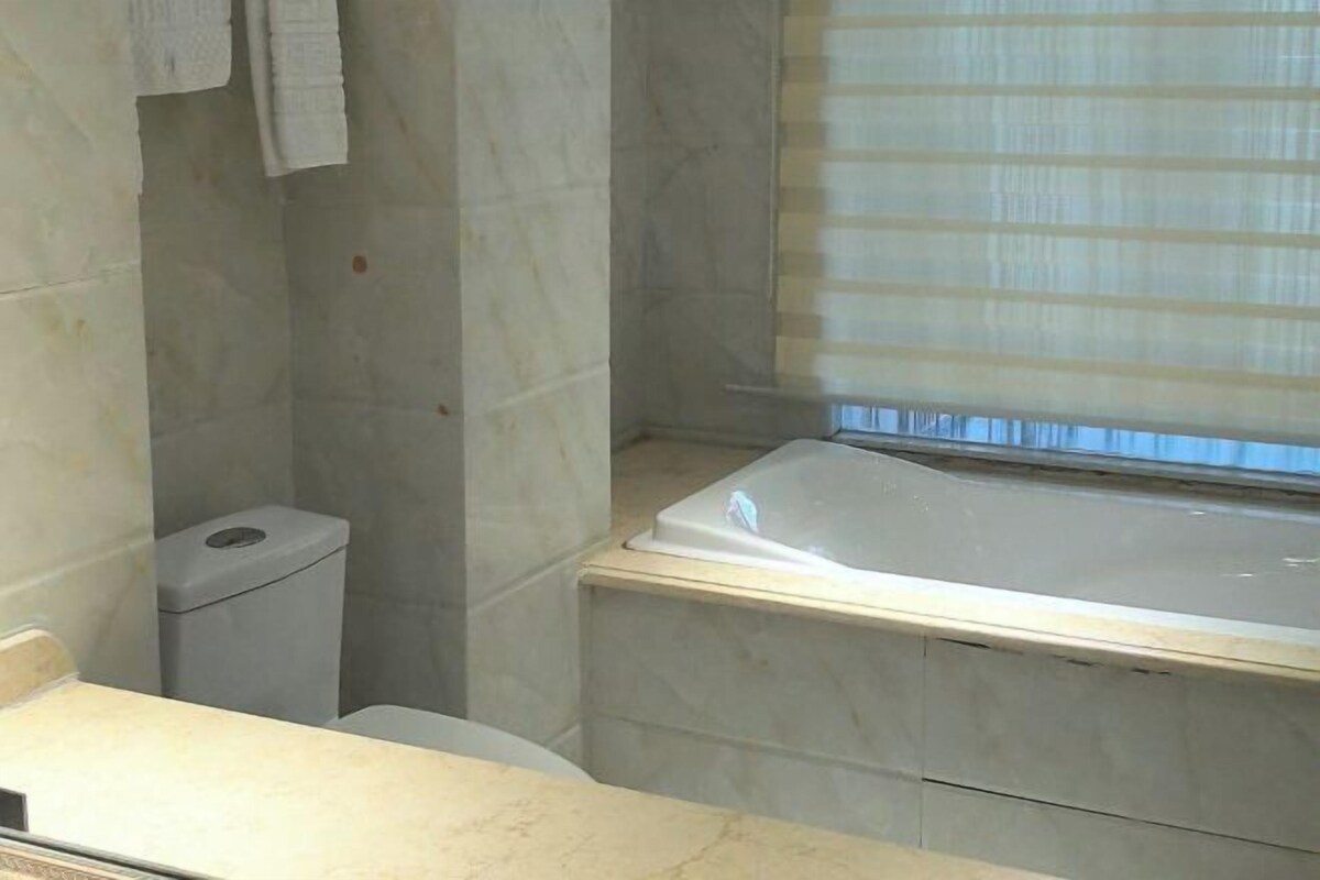A bathroom with a bathtub, toilet, and a window with blinds.