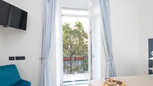 Habitación de hotel con balcón, un televisor de pantalla plana en la pared, una silla azul y una bandeja de desayuno sobre la cama.