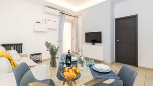 Una sala de estar moderna con comedor, un sofá, un televisor y una puerta de madera oscura.