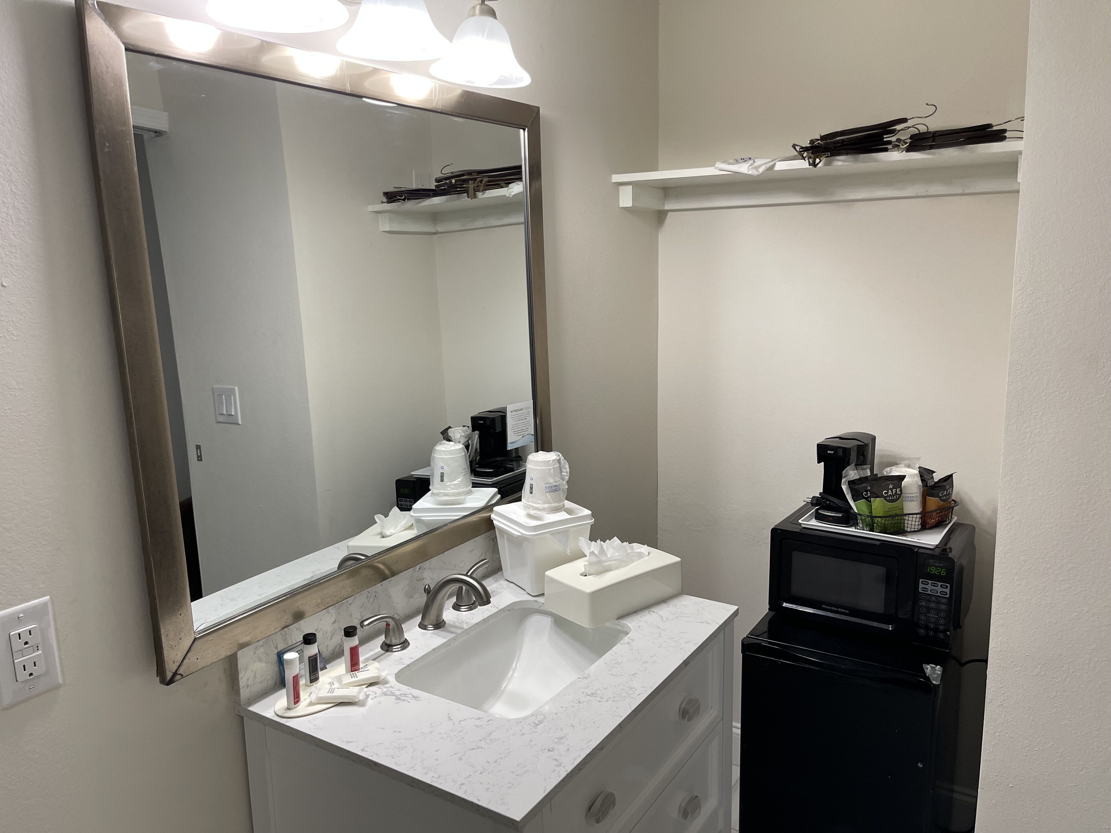 A bathroom with a large mirror, a sink, a coffee maker, and a microwave.
