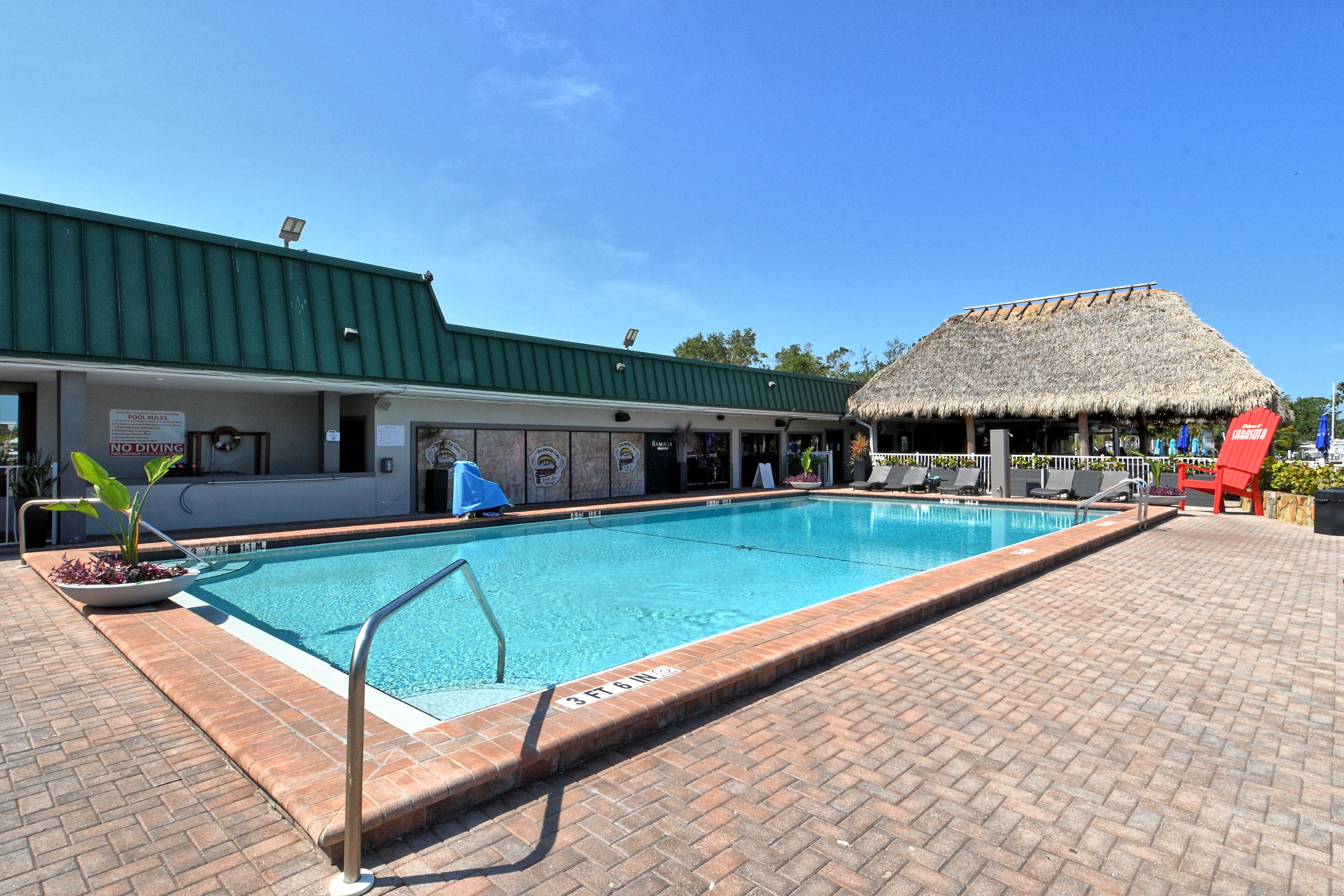 A swimming pool with a brick deck, a thatched-roof structure, and a sign indicating a pool rule.