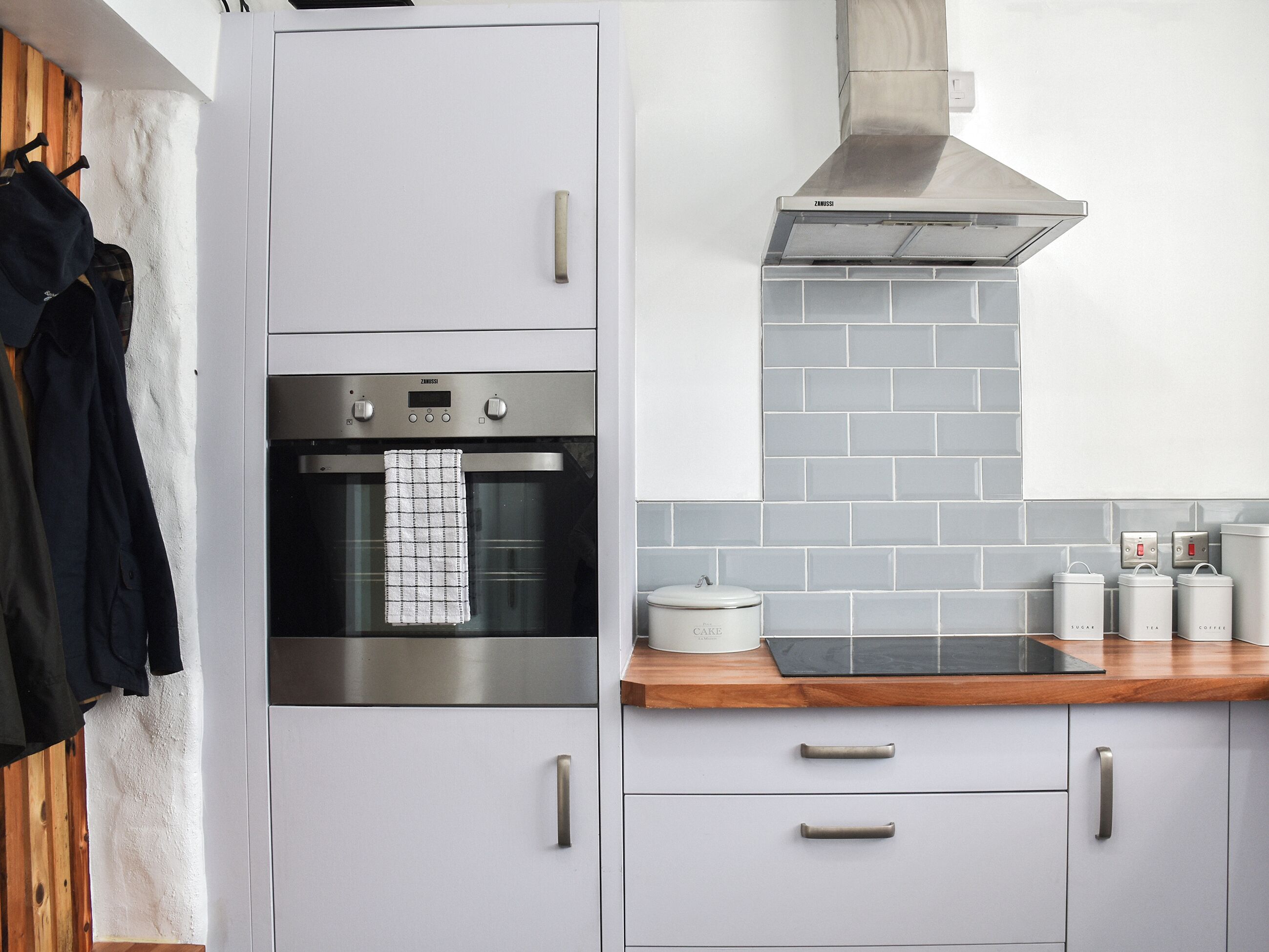 Una cucina moderna con mobili grigi, un forno in acciaio inossidabile, un piano di lavoro in legno e una parete di fondo rivestita di piastrelle grigie.