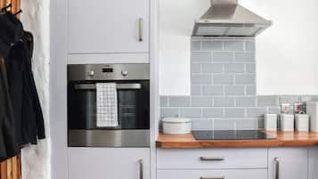 Una cucina moderna con mobili grigi, un forno in acciaio inossidabile, un piano di lavoro in legno e una parete di fondo rivestita di piastrelle grigie.