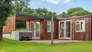 A wooden cabin with a patio, a hot tub, and a covered outdoor area.