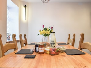 Een houten eettafel met een vaas gele bloemen, een fles melk en diverse etenswaren.