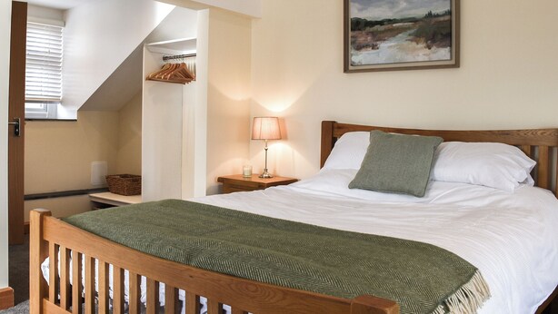A bedroom with a bed, a bedside table with a lamp, a hanging coat rack, and a painting on the wall.