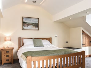 Een slaapkamer met een houten bed, een nachtkastje met een lamp, een schilderij aan de muur en een trap die naar een andere kamer leidt.