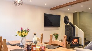 A dining area with a wooden table, chairs, a vase with flowers, jars, and a fireplace.