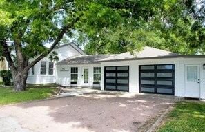 A single-story house with a garage, a driveway, and a large tree in front.